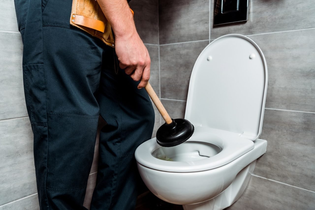 Plombier tenant une ventouse près d’un WC