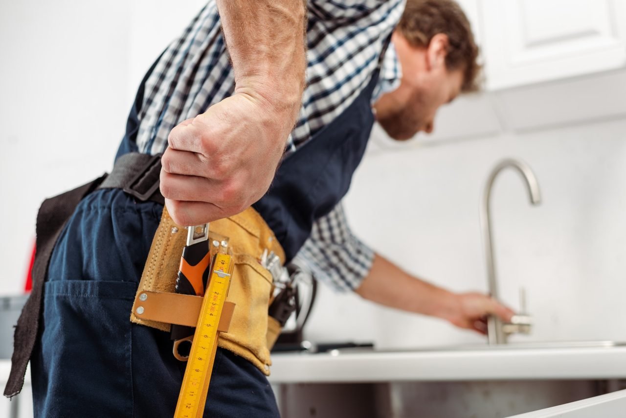 Plombier sortant une clé de sa ceinture à outils pour réparer un robinet